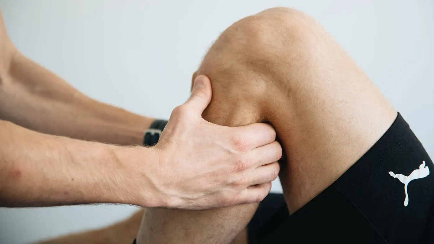Manos de un fisioterapeuta que presionan la rodilla de una persona con pantaloneta negra
