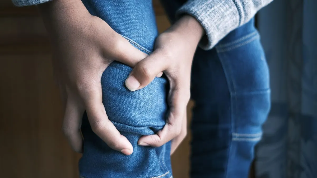 Persona de pie con jean azul que se sujeta la rodilla con las dos manos